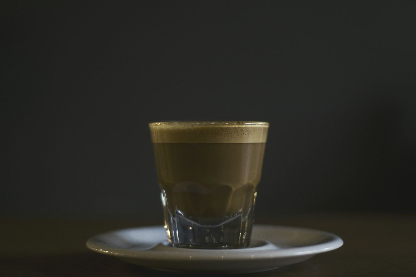 Café en vaso de cristal sobre un platillo, con el fondo oscuro