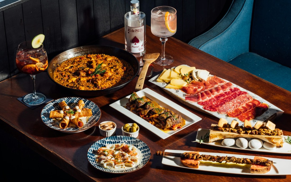 Una mesa llena para compartir: paella, jamón y embutido, quesos, tapas y bebidas