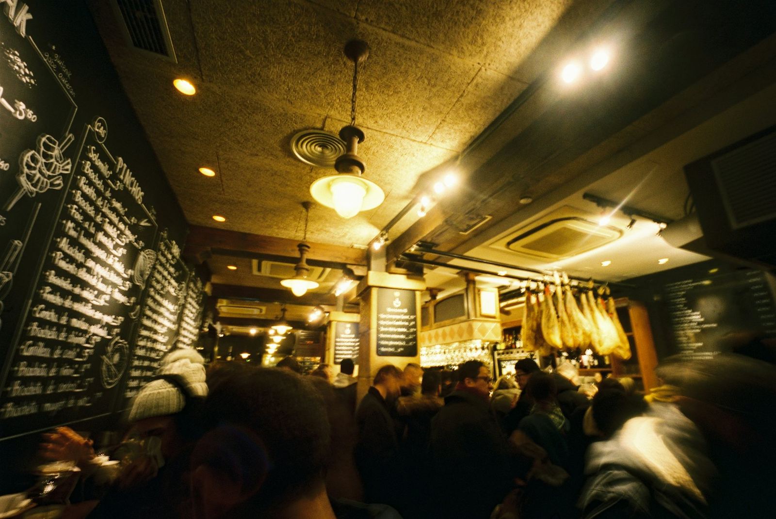 Un bar de tapas lleno de gente, con jamones colgados y pizarras escritas a tiza