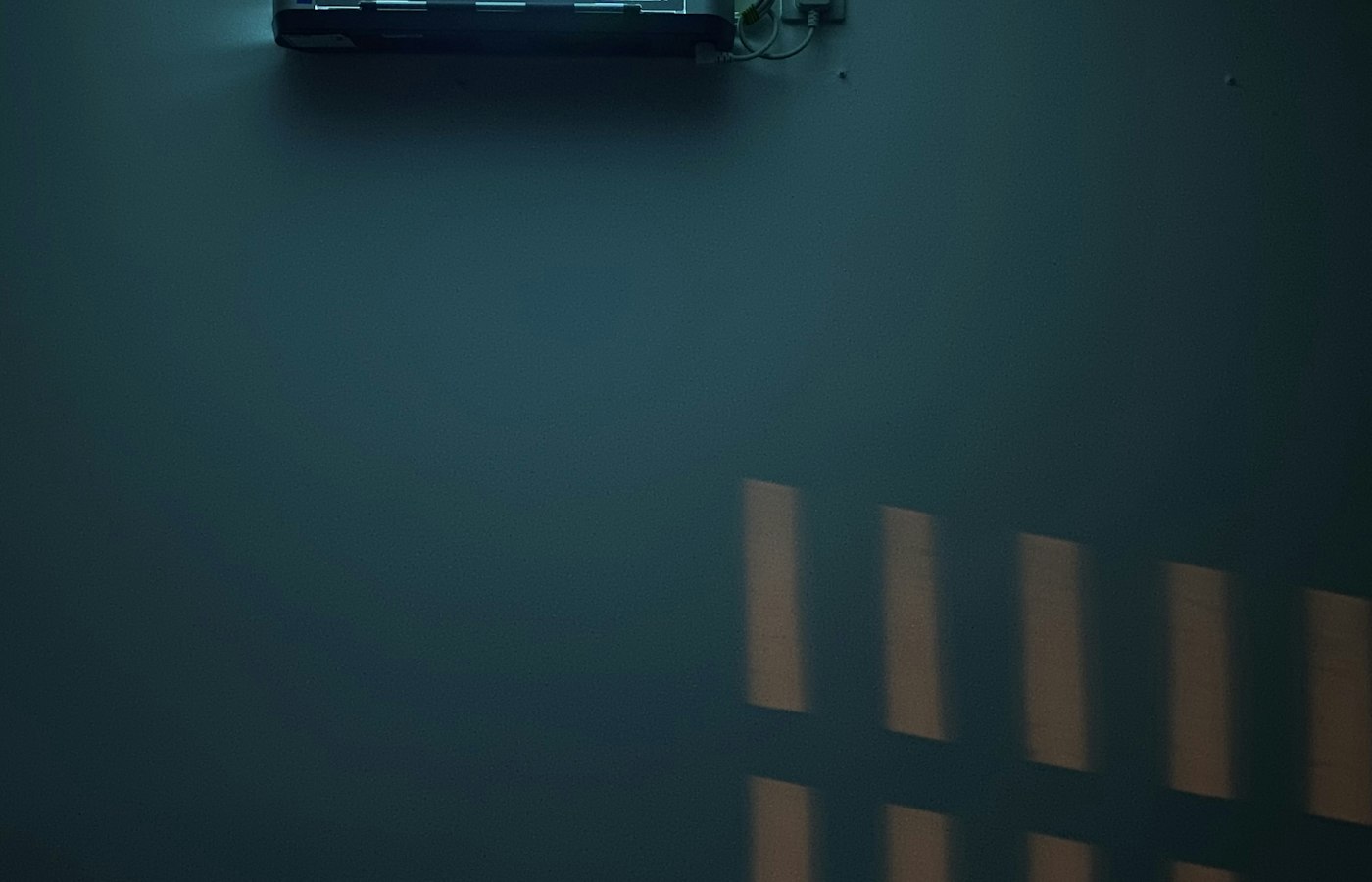 Pared oscura con un split encendido arriba y la luz de la ventana dibujada en la pared