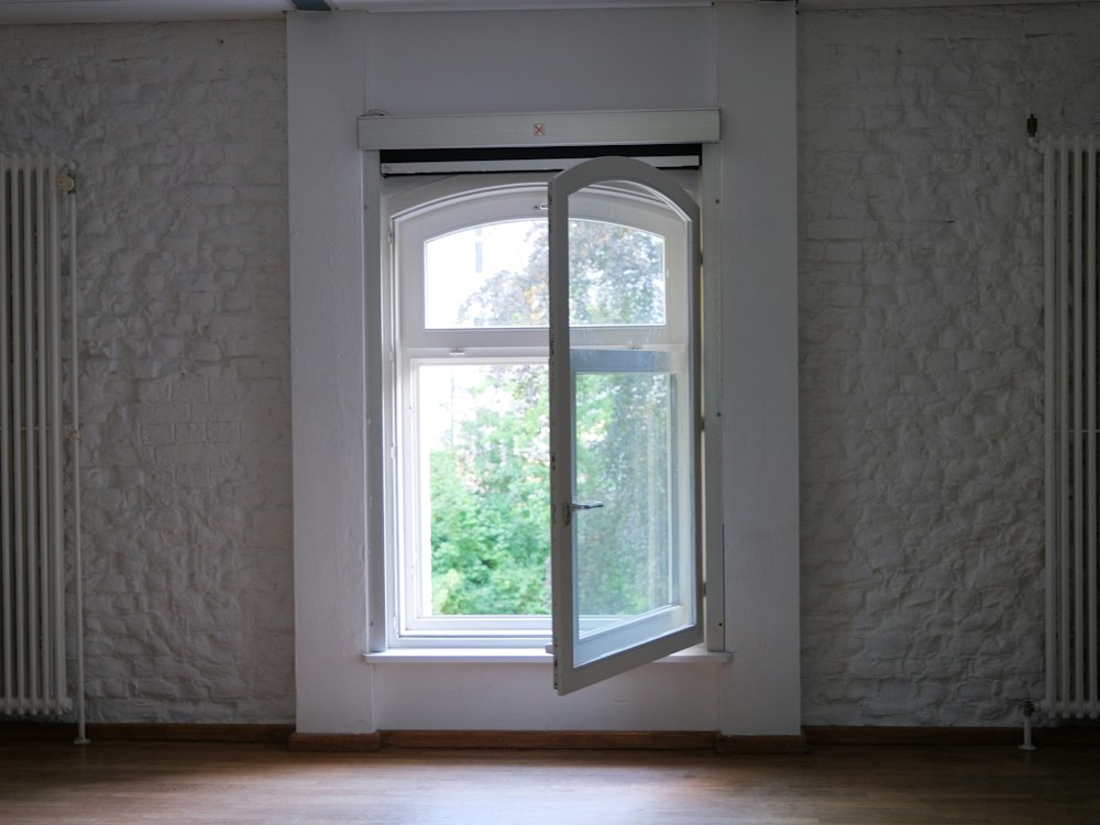 Pared blanca de ladrillo con una ventana abierta y dos radiadores antiguos a los lados