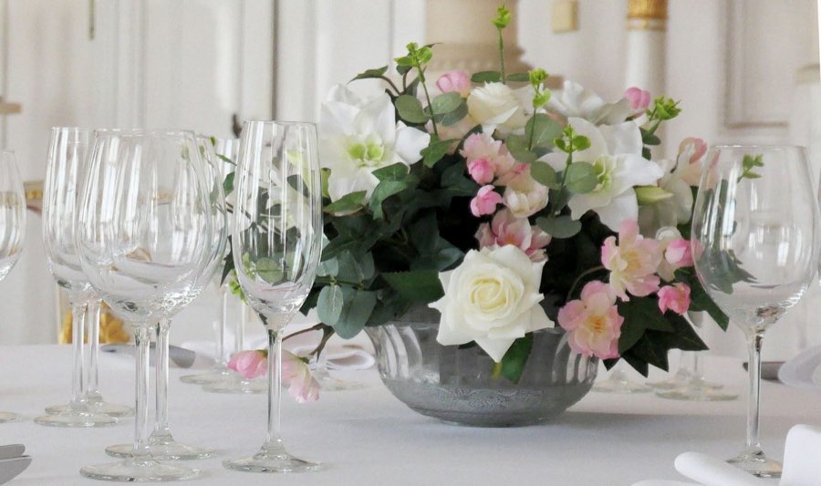 Centro bajo de rosa blanca y flor rosa en un cuenco de zinc, entre copas de cristal