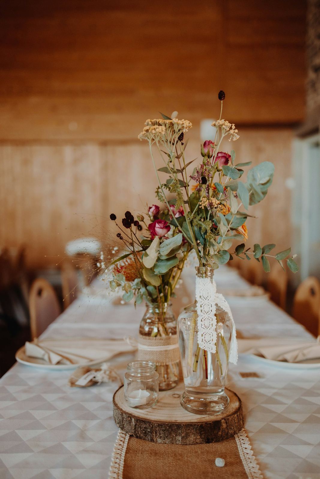Botellas de cristal con flor silvestre y encaje sobre una rodaja de tronco, en una mesa larga de banquete