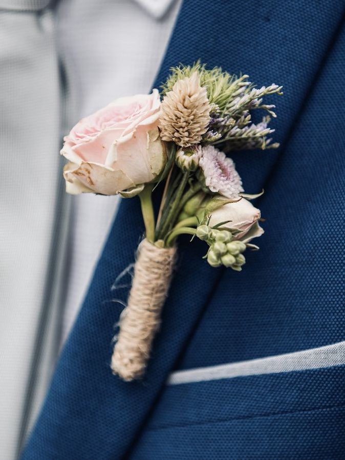 Prendido de rosa rosa y cardo, atado con yute, en la solapa de un traje azul