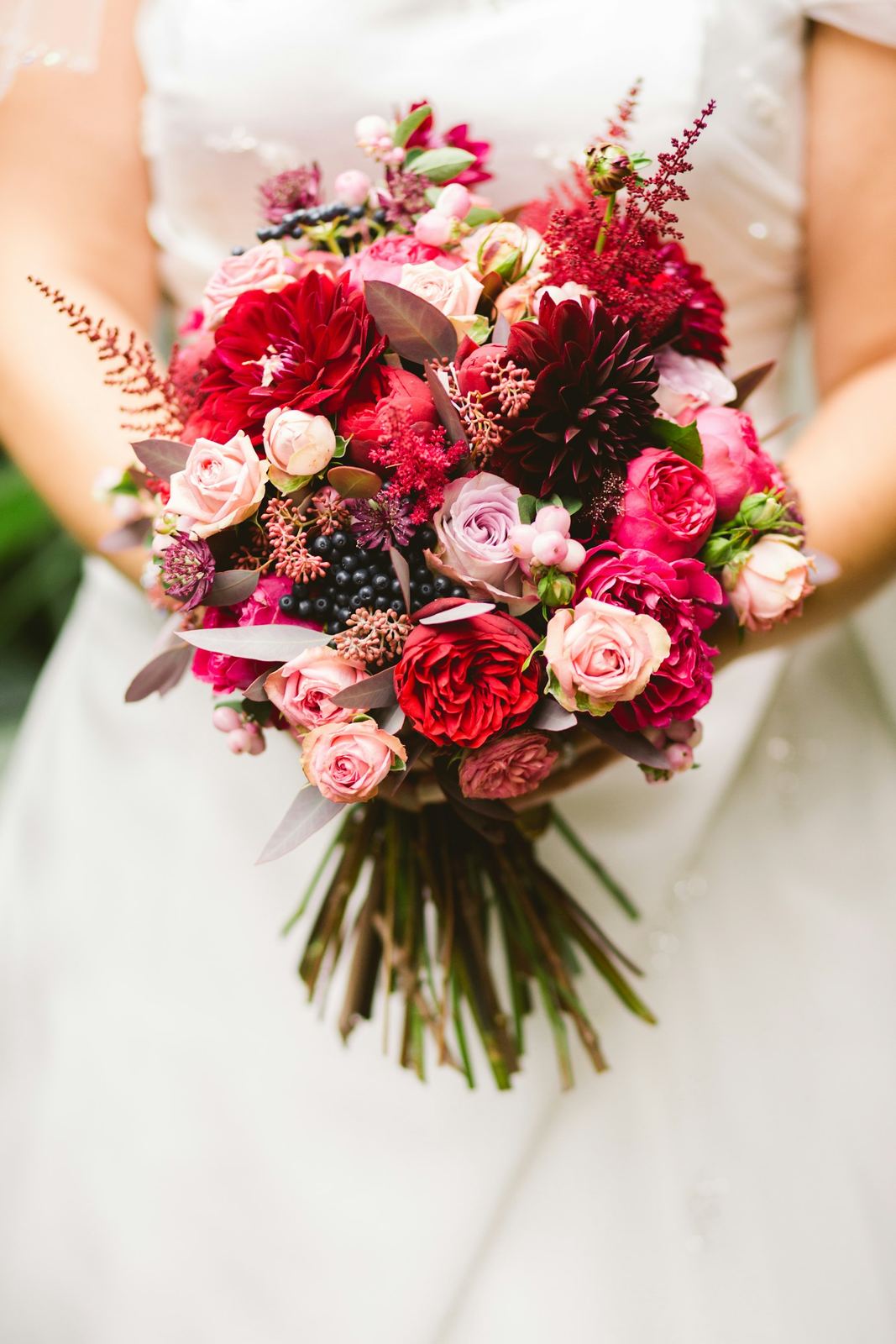 Novia sosteniendo un ramo de rosas y dalias en rojos y rosas