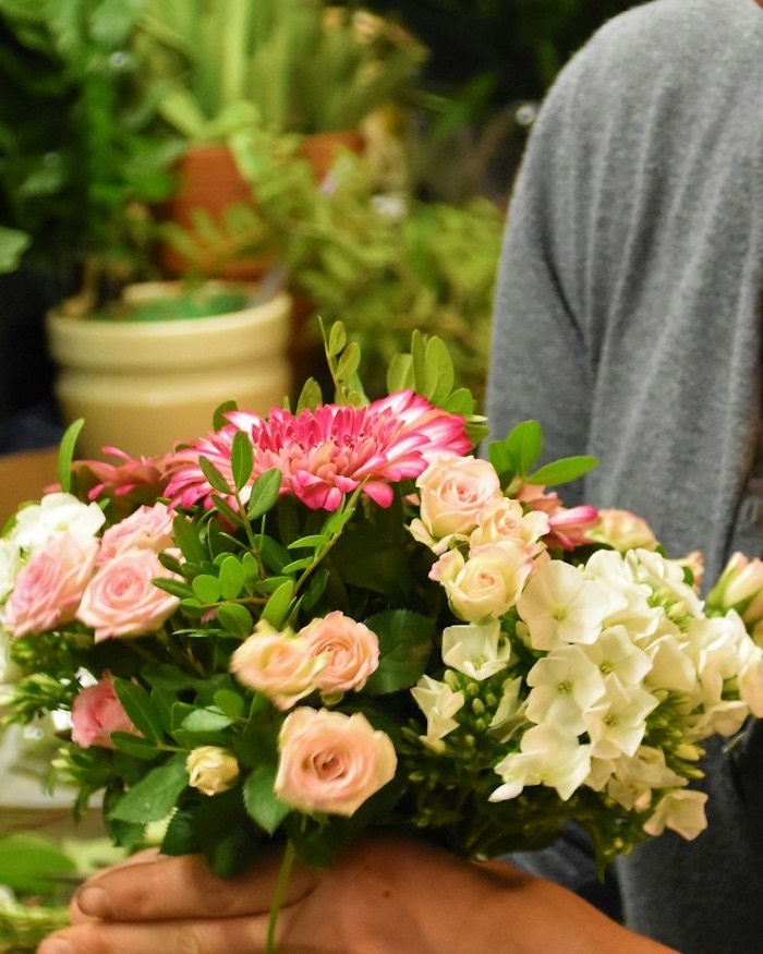 Manos sosteniendo un ramo redondo de rosas rosas, gerbera y flor blanca