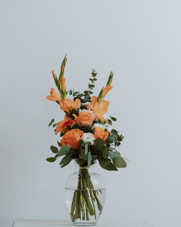 Gladiolos naranjas y rosas con eucalipto en un jarrón de cristal