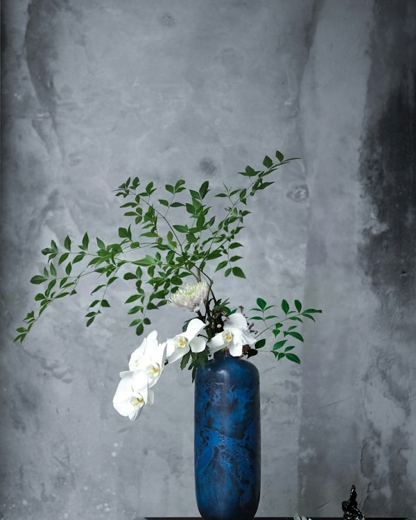 Orquídea blanca con ramas verdes en un jarrón azul