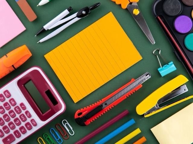 Calculadora, compás, tijeras, grapadora, acuarelas y lápices sobre un fondo verde