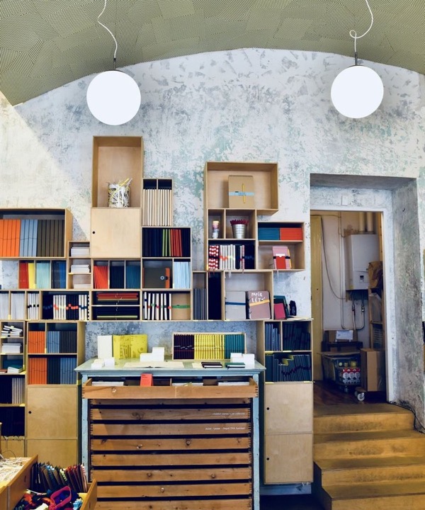 Estanterías de madera con cuadernos de colores y un mueble de cajones bajo un techo abovedado